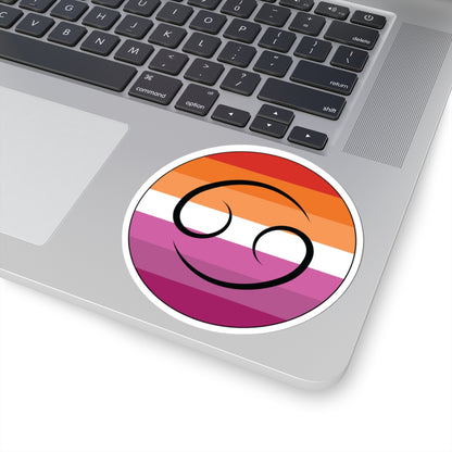 Close-up of the bottom right corner of a silver laptop featuring a 4 inch by 4 inch circular zodiac sticker with a centered Cancer glyph on a Lesbian pride flag style background applied to the surface.