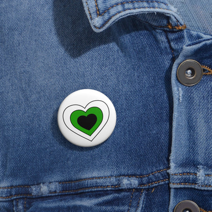 Close-up of a white circular pride button featuring a nested heart design inspired by the Neutrois pride flag in white, green and black, attached to a blue denim jacket at the right chest with the button clearly visible.