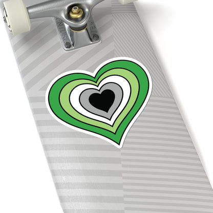 Close-up of the bottom of a silver laptop featuring a 6 inch by 6 inch pride flag heart sticker in an Aromantic flag style applied to the surface.