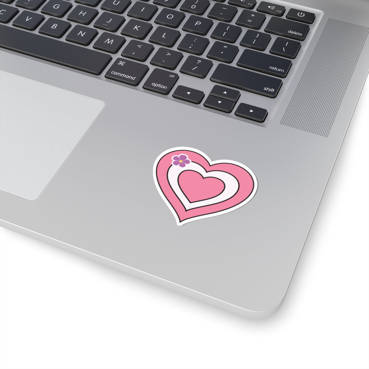 Close-up of the bottom right corner of a silver laptop featuring a 2 inch by 2 inch pride flag heart sticker in a Sapphic pride flag style applied to the surface.