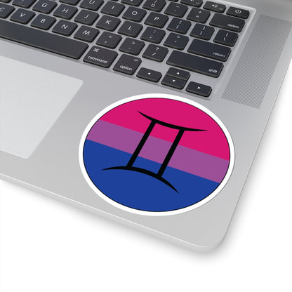 Close-up of the bottom right corner of a silver laptop featuring a 4 inch by 4 inch circular zodiac sticker with a centered Gemini glyph on a Bisexual pride flag style background applied to the surface.