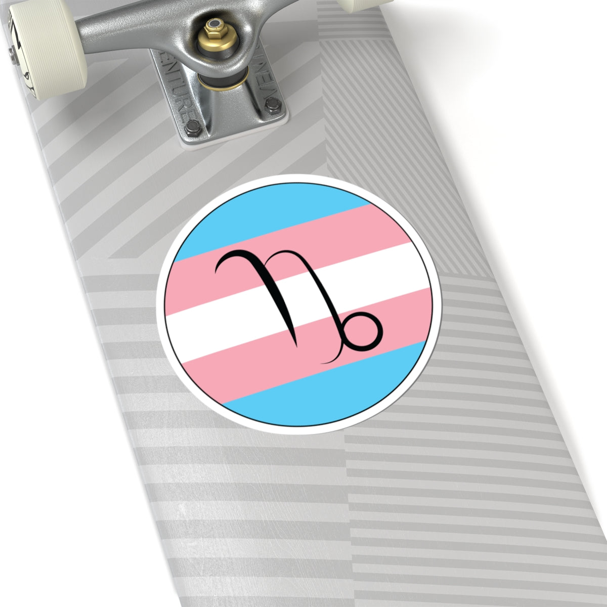 Close-up of the bottom of a silver skateboard featuring a 6 inch by 6 inch circular zodiac sticker with a centered Capricorn glyph on a Transgender pride flag style background applied to the surface.