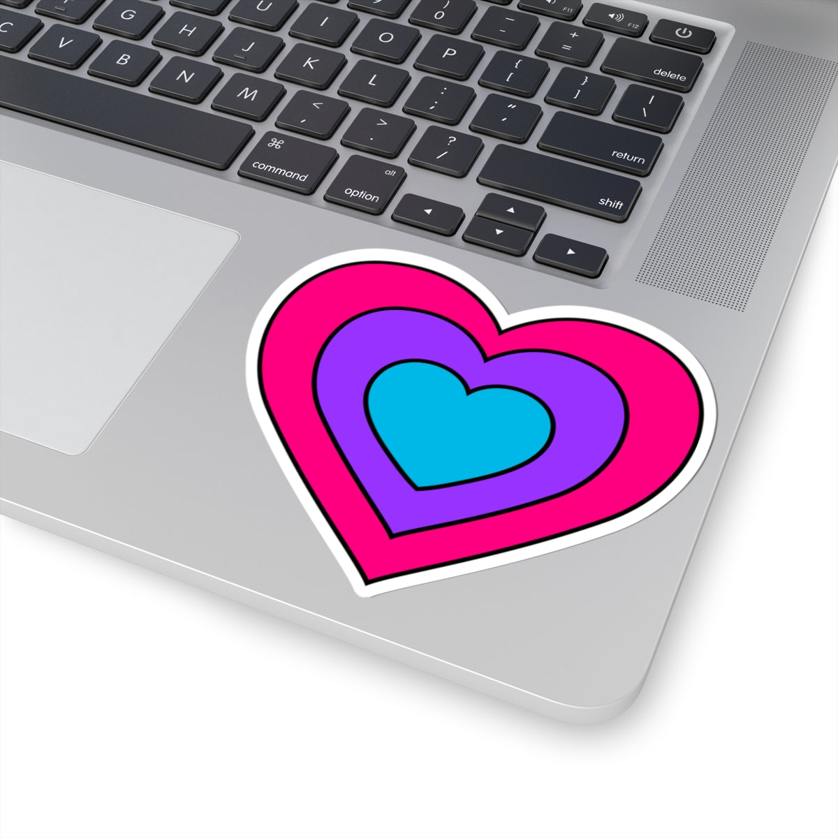 Close-up of the bottom right corner of a silver laptop featuring a 4 inch by 4 inch pride flag heart sticker in an Androgyne flag style applied to the surface.