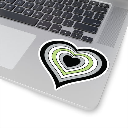 Close-up of the bottom right corner of a silver laptop featuring a 4 inch by 4 inch pride flag heart sticker in an Agender flag style applied to the surface.