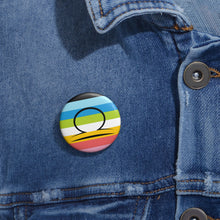 Close-up of a white circular pride button featuring the Libra zodiac glyph centered over a queer pride flag background in pinks, yellow, white, green, blues, and black, attached to a blue denim jacket at the right chest with the button clearly visible.