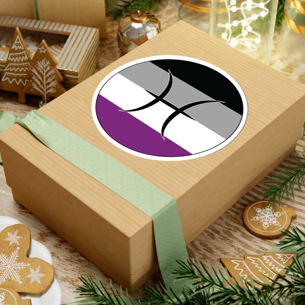 Gift box with a green ribbon on a festive background with cookies and Christmas decorations. Pisces Asexual pride sticker centered on the box.