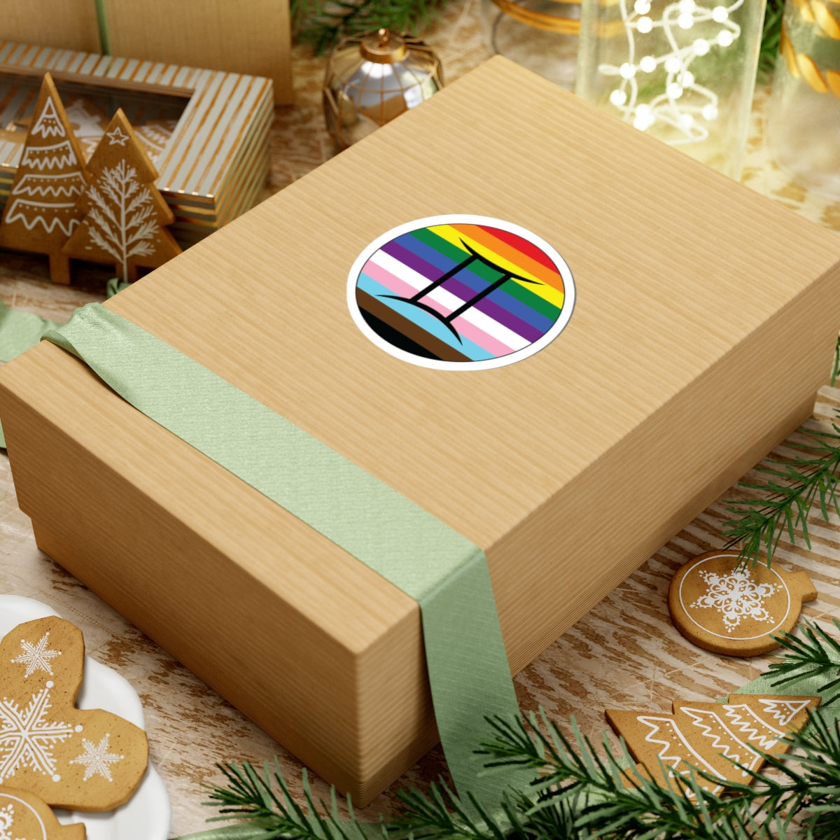 Gift box with a green ribbon on a festive background with cookies and Christmas decorations. Gemini Progress pride sticker centered on the box.
