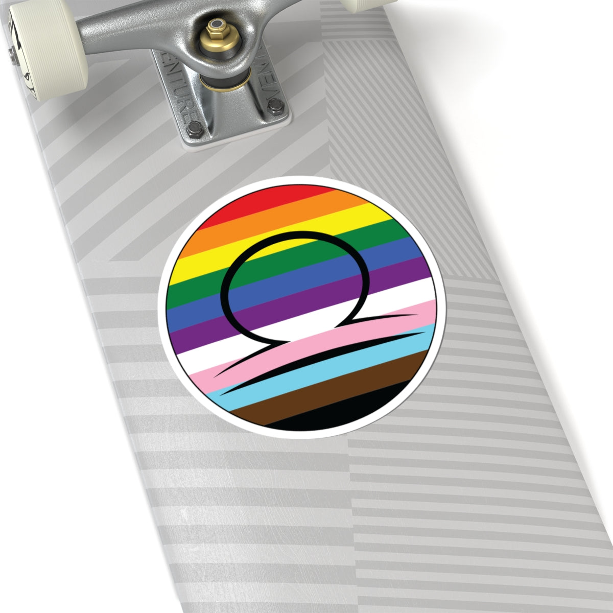 Close-up of the bottom of a silver skateboard featuring a 2 inch by 2 inch circular zodiac sticker with a centered Libra glyph on a progress pride flag style background applied to the surface.