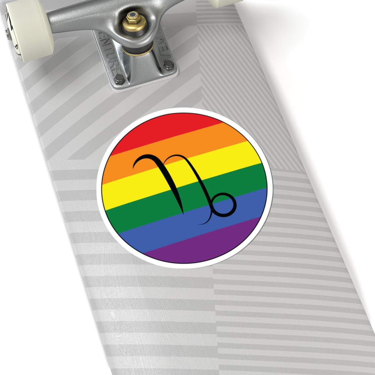 Close-up of the bottom of a silver skateboard featuring a 6 inch by 6 inch circular zodiac sticker with a centered Capricorn glyph on a Rainbow pride flag style background applied to the surface.