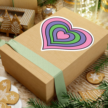 Gift box with a green ribbon on a festive background with cookies and Christmas decorations. Heart-shaped Trigender pride sticker centered on the box.