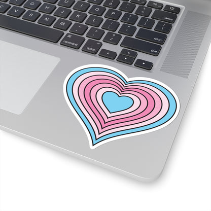 Close-up of the bottom right corner of a silver laptop featuring a 4 inch by 4 inch pride flag heart sticker in a Transfem flag style applied to the surface.