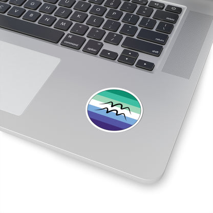 Close-up of the bottom right corner of a silver laptop featuring a 2 inch by 2 inch circular zodiac sticker with a centered Aquarius glyph on a Gay Men pride flag style background applied to the surface.