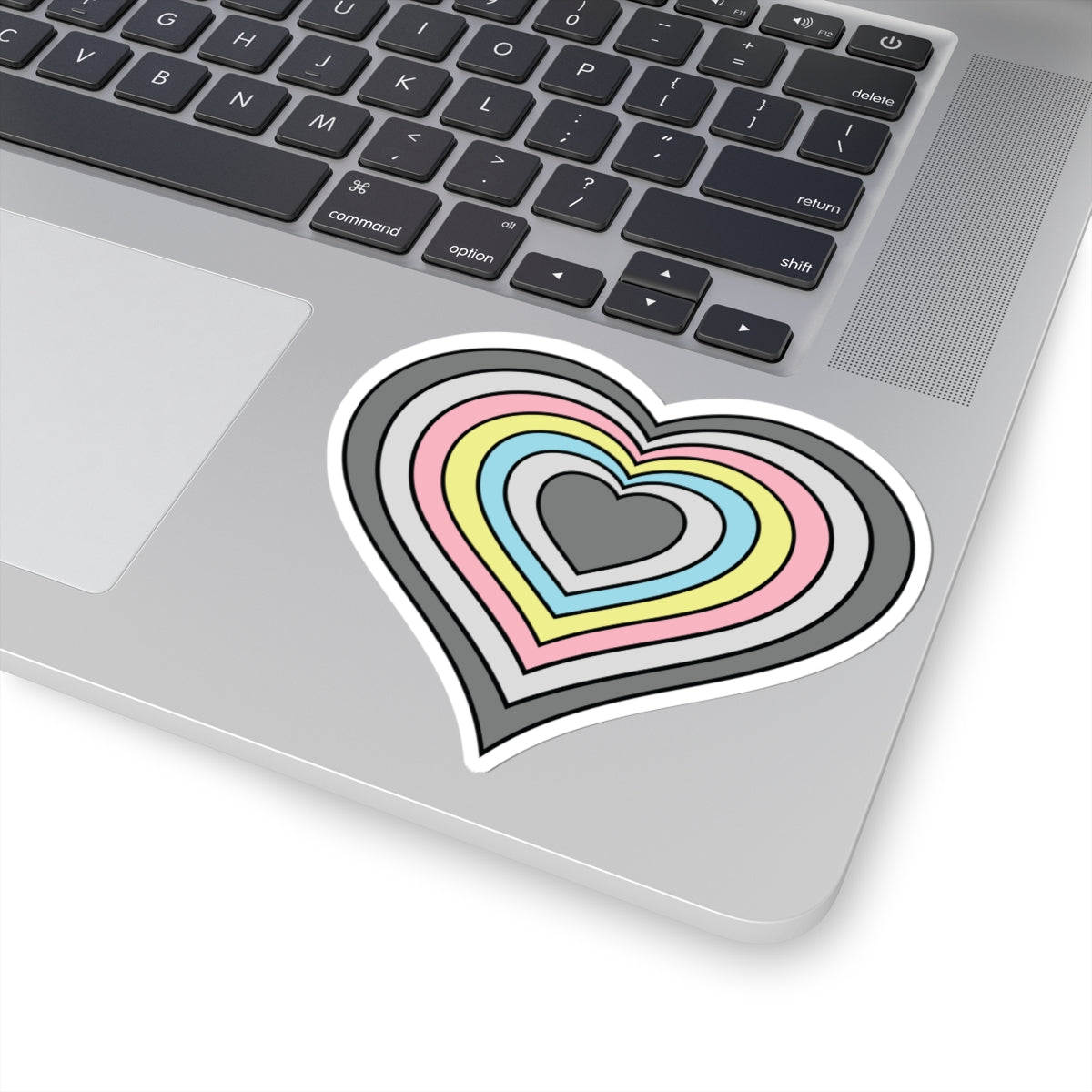 Close-up of the bottom right corner of a silver laptop featuring a 4 inch by 4 inch pride flag heart sticker in a Demiflux flag style applied to the surface.
