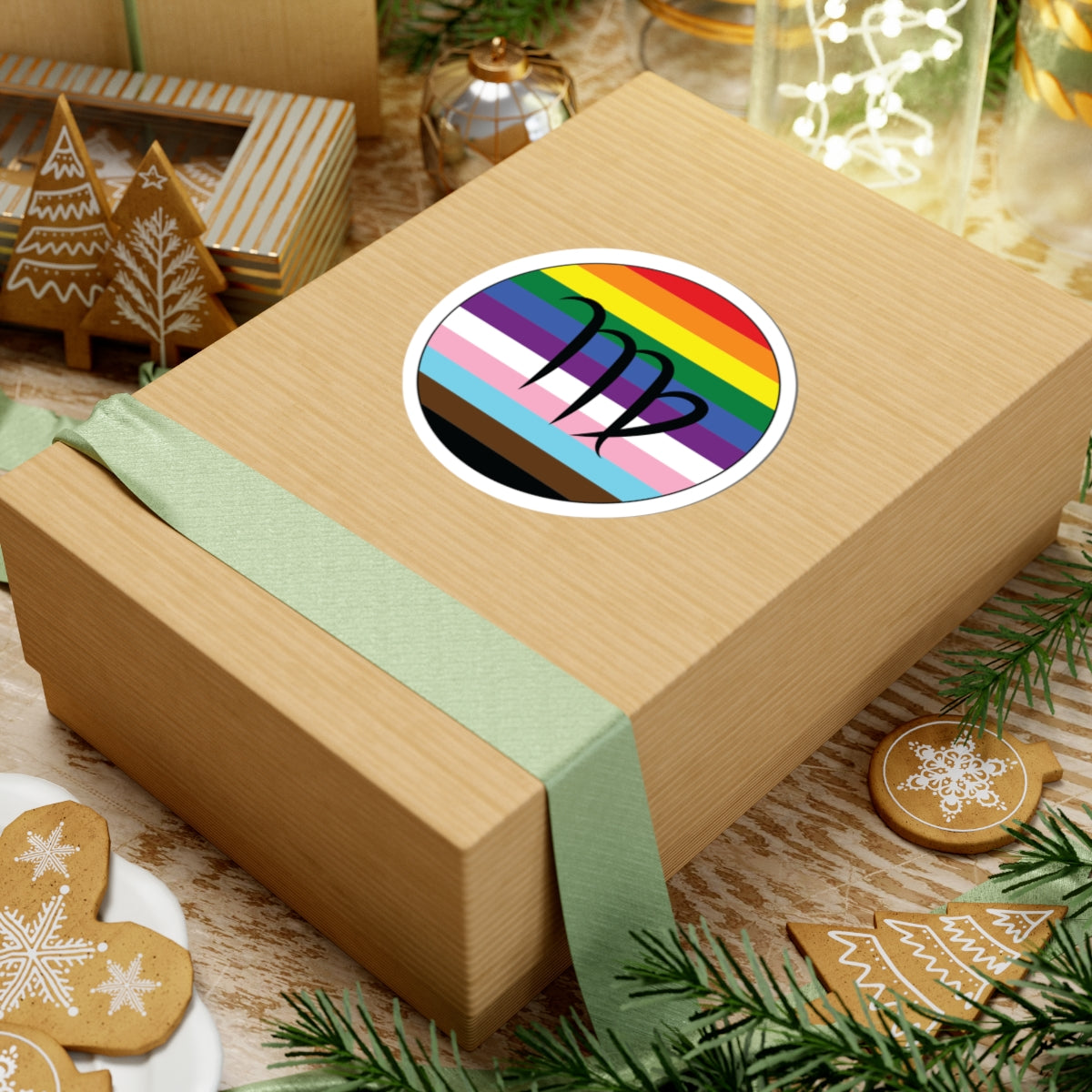 Gift box with a green ribbon on a festive background with cookies and Christmas decorations. Virgo Progress pride sticker centered on the box.