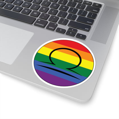 Close-up of the bottom right corner of a silver laptop featuring a 4 inch by 4 inch circular zodiac sticker with a centered Libra glyph on a Rainbow pride flag style background applied to the surface.