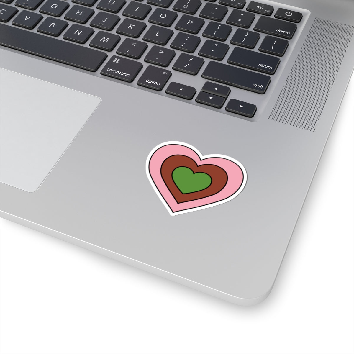 Close-up of the bottom right corner of a silver laptop featuring a 2 inch by 2 inch pride flag heart sticker in a Gynesexual flag style applied to the surface.