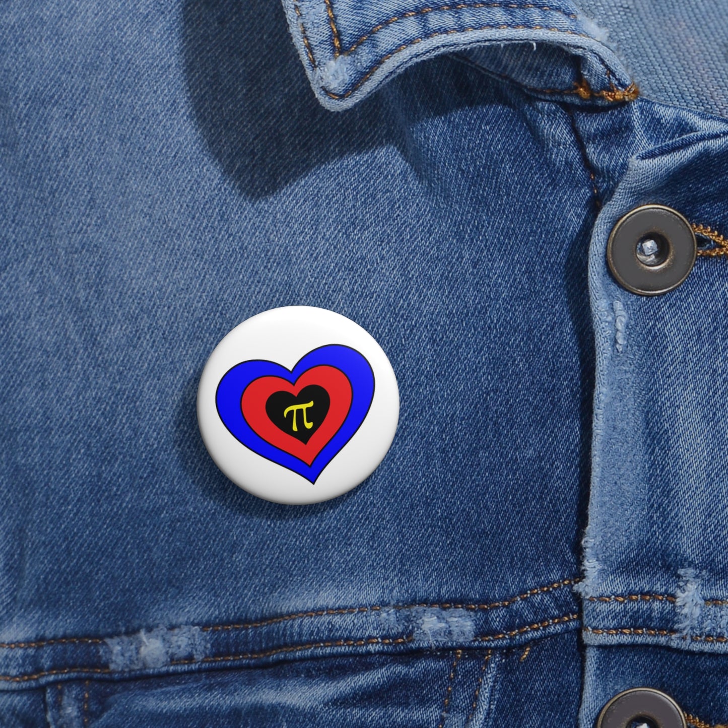 Close-up of a white circular pride button featuring a nested heart design inspired by the Polyamory pride flag in blue, red, black and yellow, attached to a blue denim jacket at the right chest with the button clearly visible.