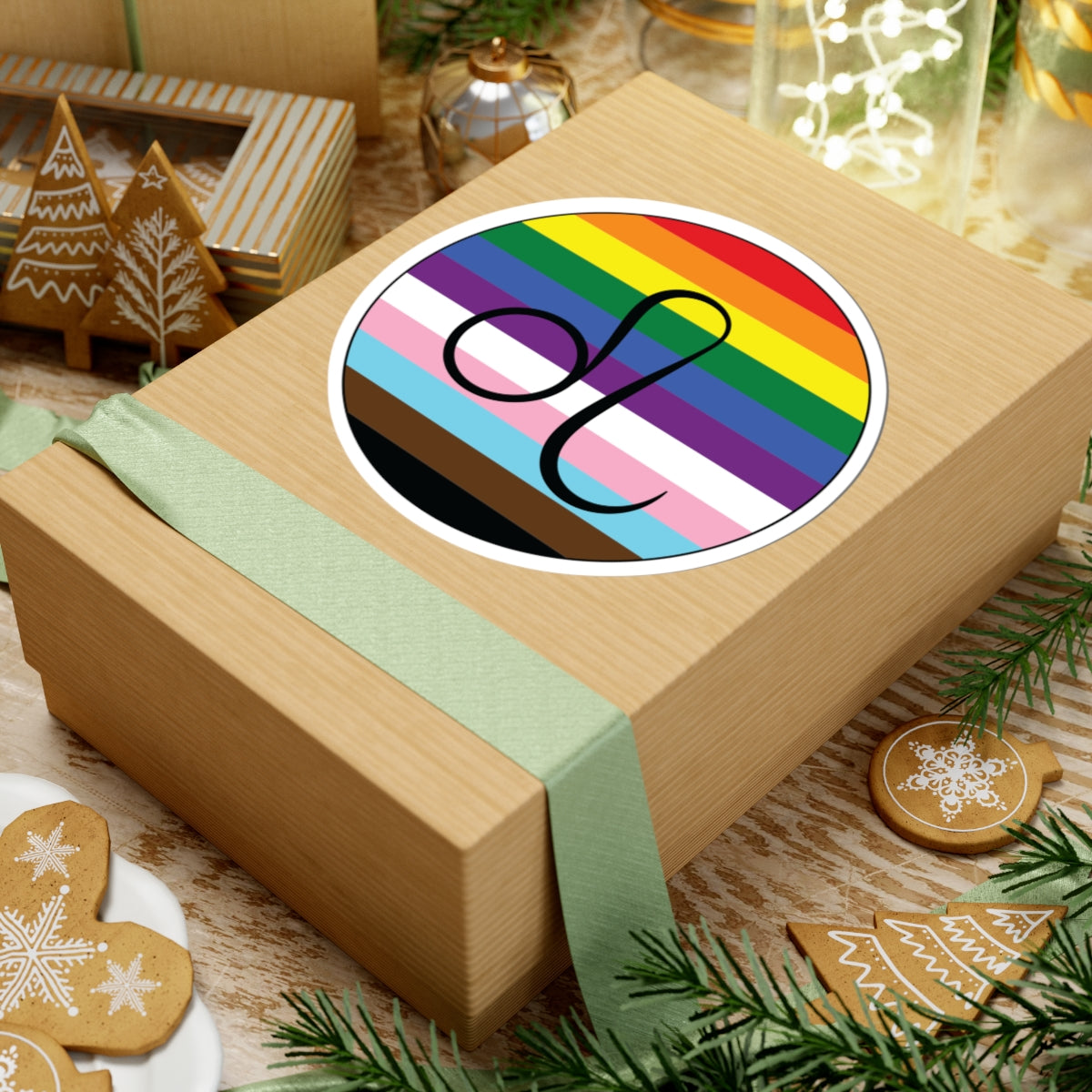 Gift box with a green ribbon on a festive background with cookies and Christmas decorations. Leo Progress pride sticker centered on the box.
