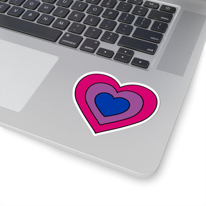 Close-up of the bottom right corner of a silver laptop featuring a 3 inch by 3 inch pride flag heart sticker in a Bisexual flag style applied to the surface.