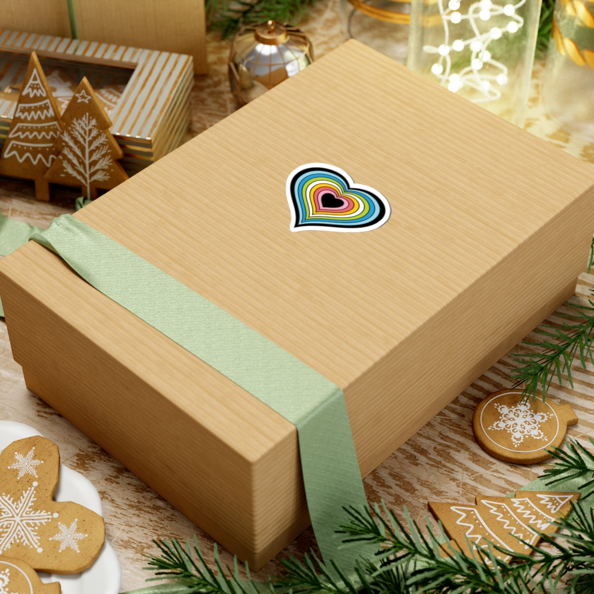 Gift box with a green ribbon on a festive background with cookies and Christmas decorations. Heart-shaped Queer pride sticker centered on the box.
