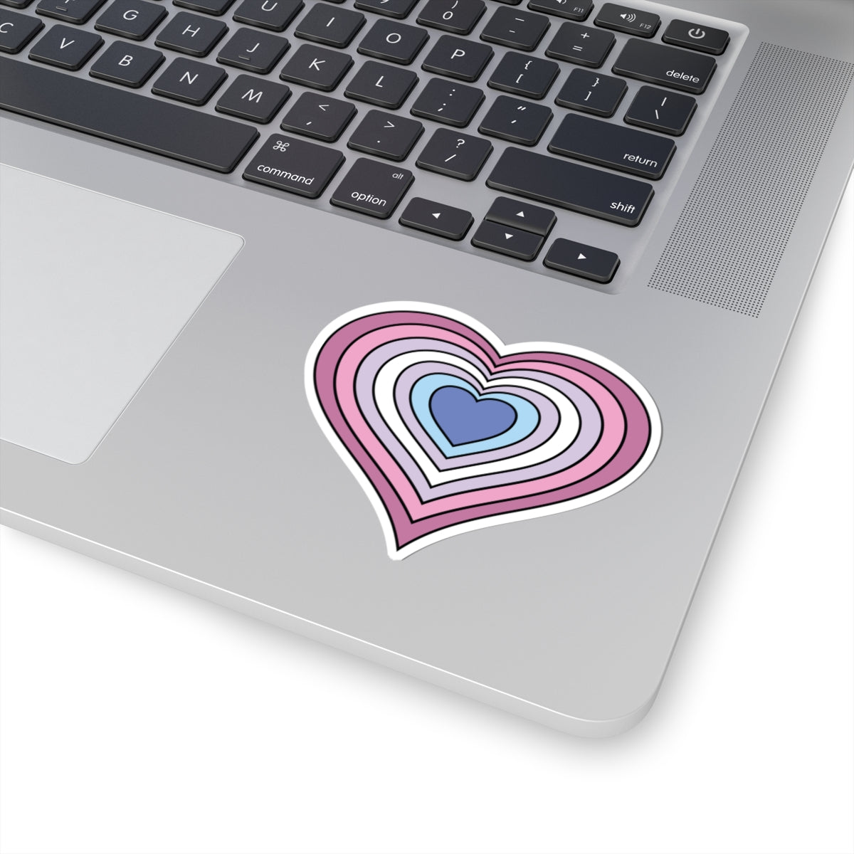 Close-up of the bottom right corner of a silver laptop featuring a 3 inch by 3 inch pride flag heart sticker in a Bigender flag style applied to the surface.
