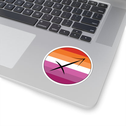 Close-up of the bottom right corner of a silver laptop featuring a 3 inch by 3 inch circular zodiac sticker with a centered Sagittarius glyph on a Lesbian pride flag style background applied to the surface.