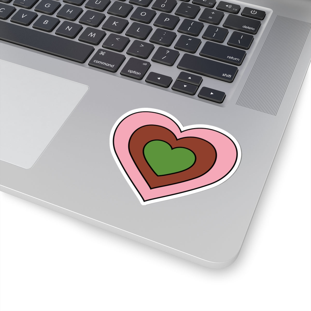 Close-up of the bottom right corner of a silver laptop featuring a 3 inch by 3 inch pride flag heart sticker in a Gynesexual flag style applied to the surface.
