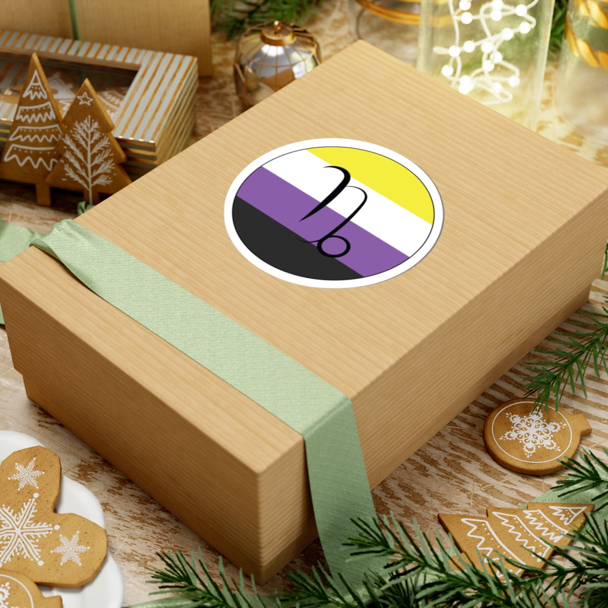 Gift box with a green ribbon on a festive background with cookies and Christmas decorations. Capricorn Nonbinary pride sticker centered on the box.