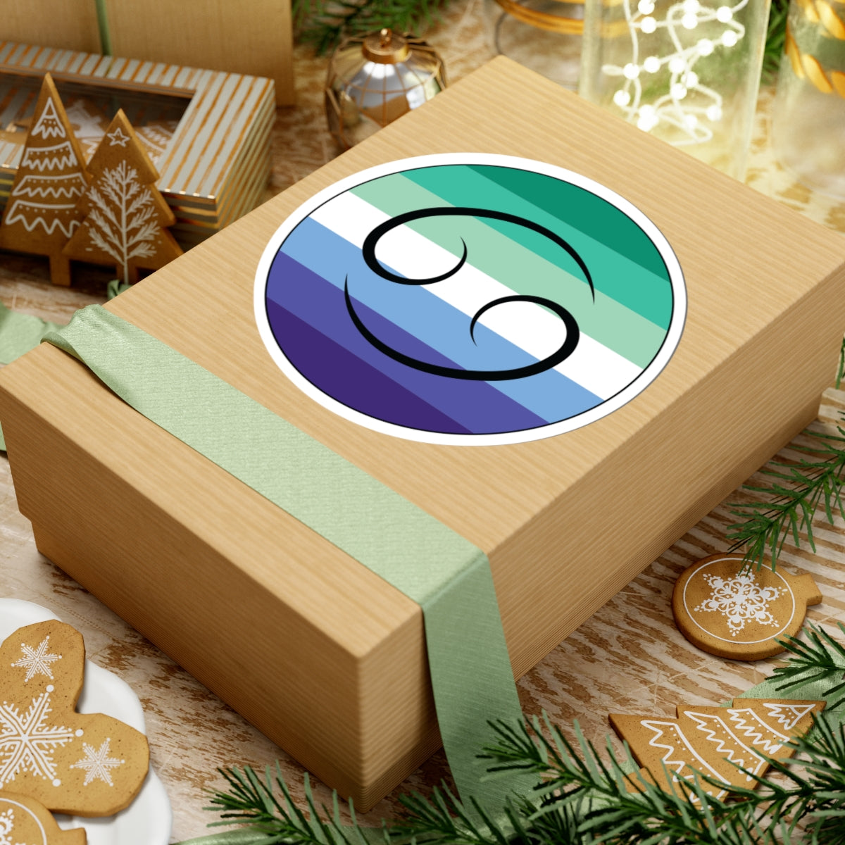 Gift box with a green ribbon on a festive background with cookies and Christmas decorations. Cancer Gay Men pride sticker centered on the box.