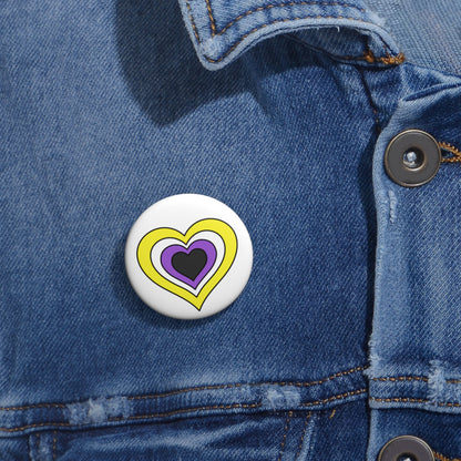 Close-up of a white circular pride button featuring a nested heart design inspired by the Nonbinary pride flag in yellow, white, purple and dark gray, attached to a blue denim jacket at the right chest with the button clearly visible.