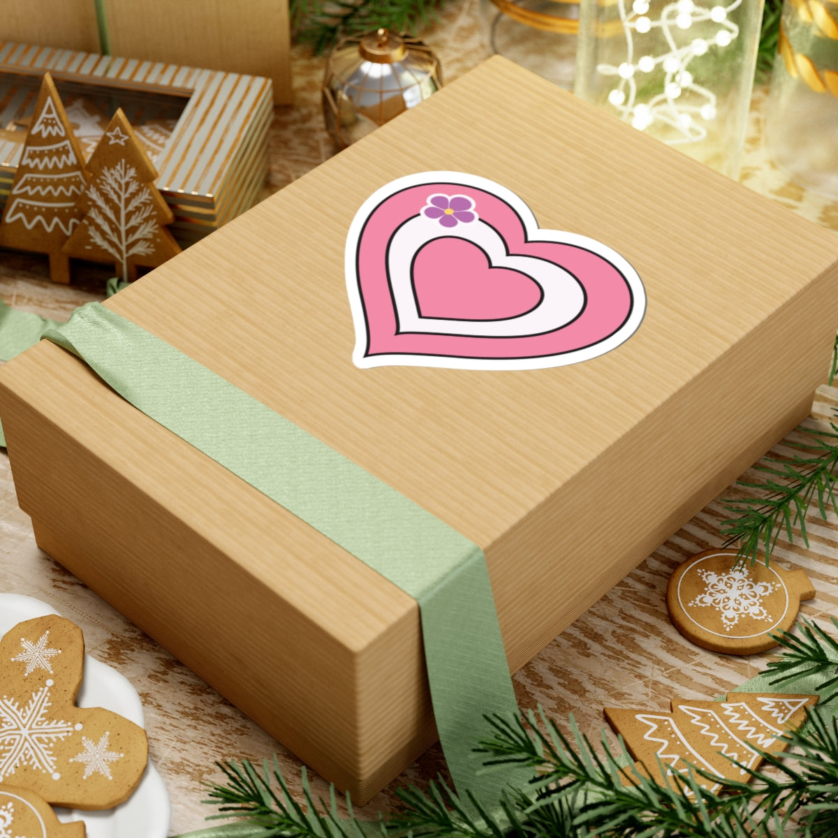 Gift box with a green ribbon on a festive background with cookies and Christmas decorations. Sapphic pride heart sticker centered on the box.