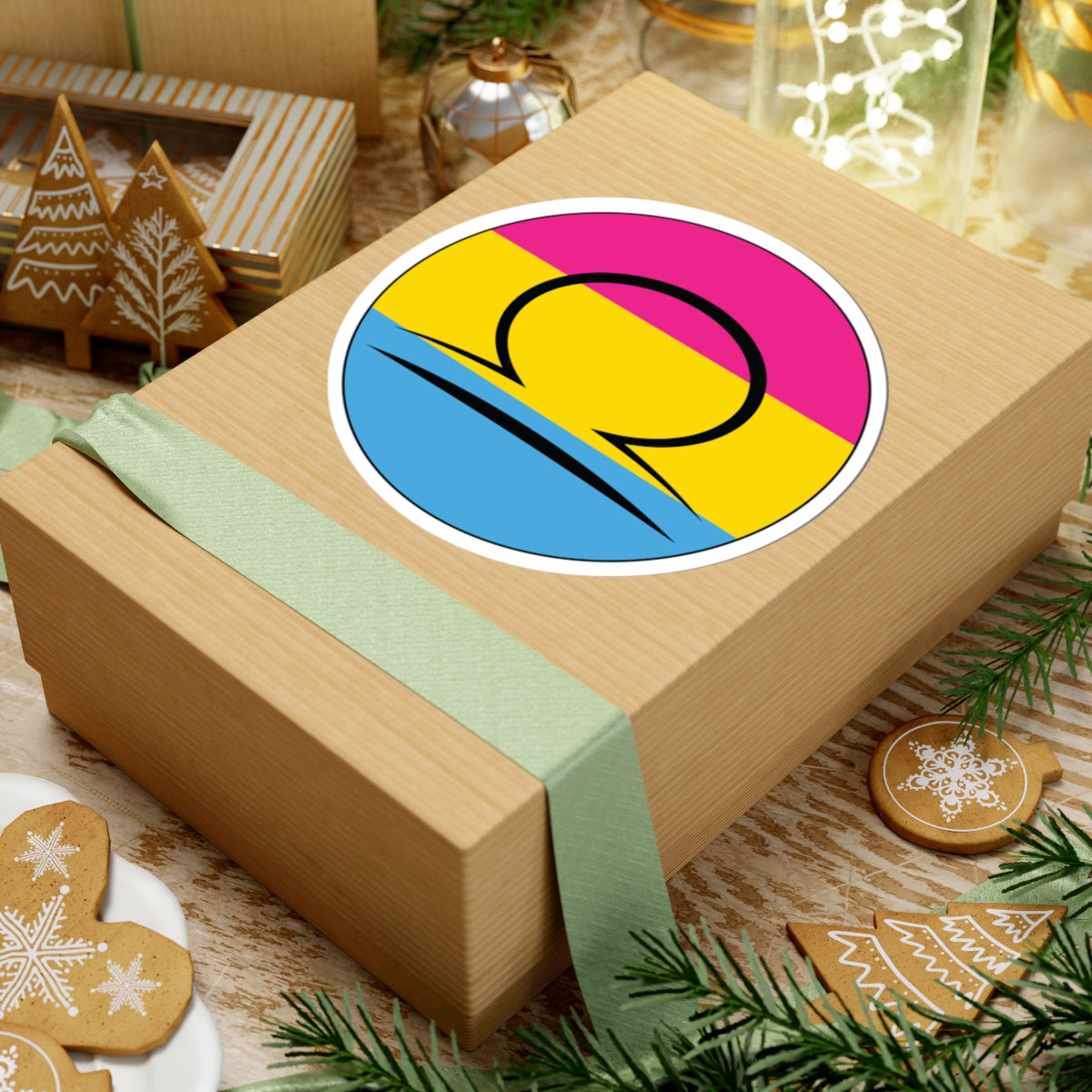 Gift box with a green ribbon on a festive background with cookies and Christmas decorations. Libra Pansexual pride sticker centered on the box.
