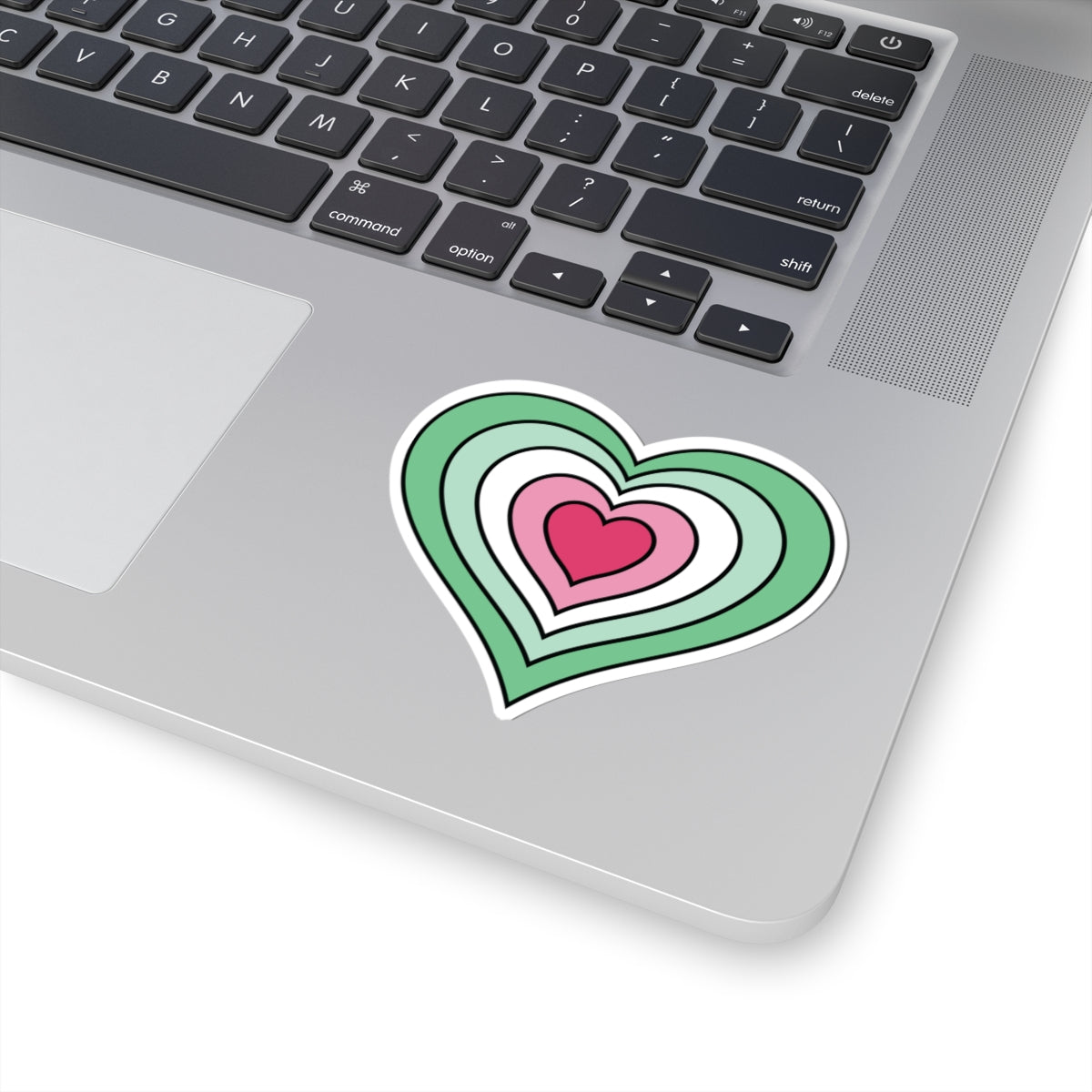 Close-up of the bottom right corner of a silver laptop featuring a 3 inch by 3 inch pride flag heart sticker in an Abrosexual flag style applied to the surface.