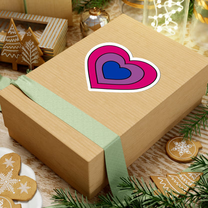 Gift box with a green ribbon on a festive background with cookies and Christmas decorations. Heart-shaped Bisexual pride sticker centered on the box.