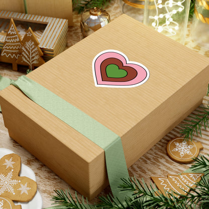 Gift box with a green ribbon on a festive background with cookies and Christmas decorations. Heart-shaped Gynesexual pride sticker centered on the box.