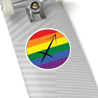 Close-up of the bottom right corner of a silver laptop featuring a 6 inch by 6 inch circular zodiac sticker with a centered Sagittarius glyph on a Rainbow pride flag style background applied to the surface.