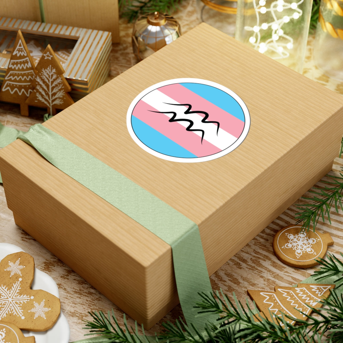 Gift box with a green ribbon on a festive background with cookies and Christmas decorations. Aquarius Transgender pride sticker centered on the box.