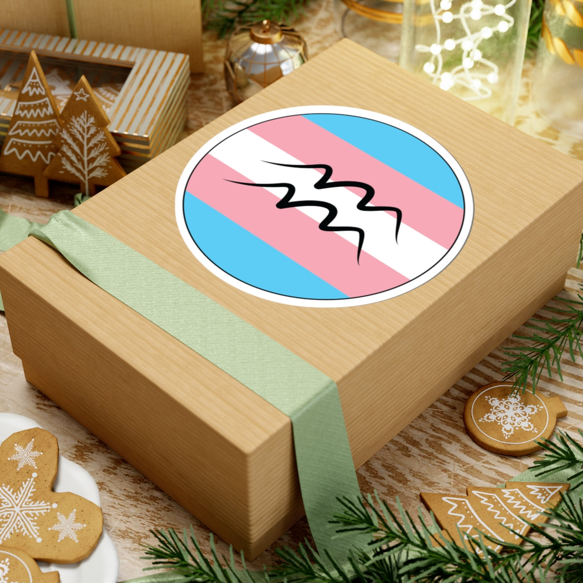 Gift box with a green ribbon on a festive background with cookies and Christmas decorations. Aquarius Transgender pride sticker centered on the box.