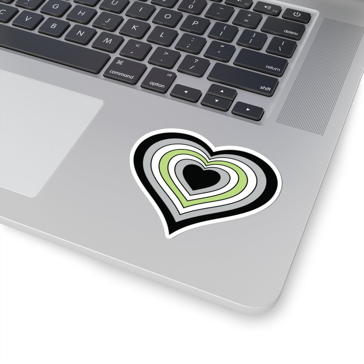 Close-up of the bottom right corner of a silver laptop featuring a 3 inch by 3 inch pride flag heart sticker in an Agender flag style applied to the surface.