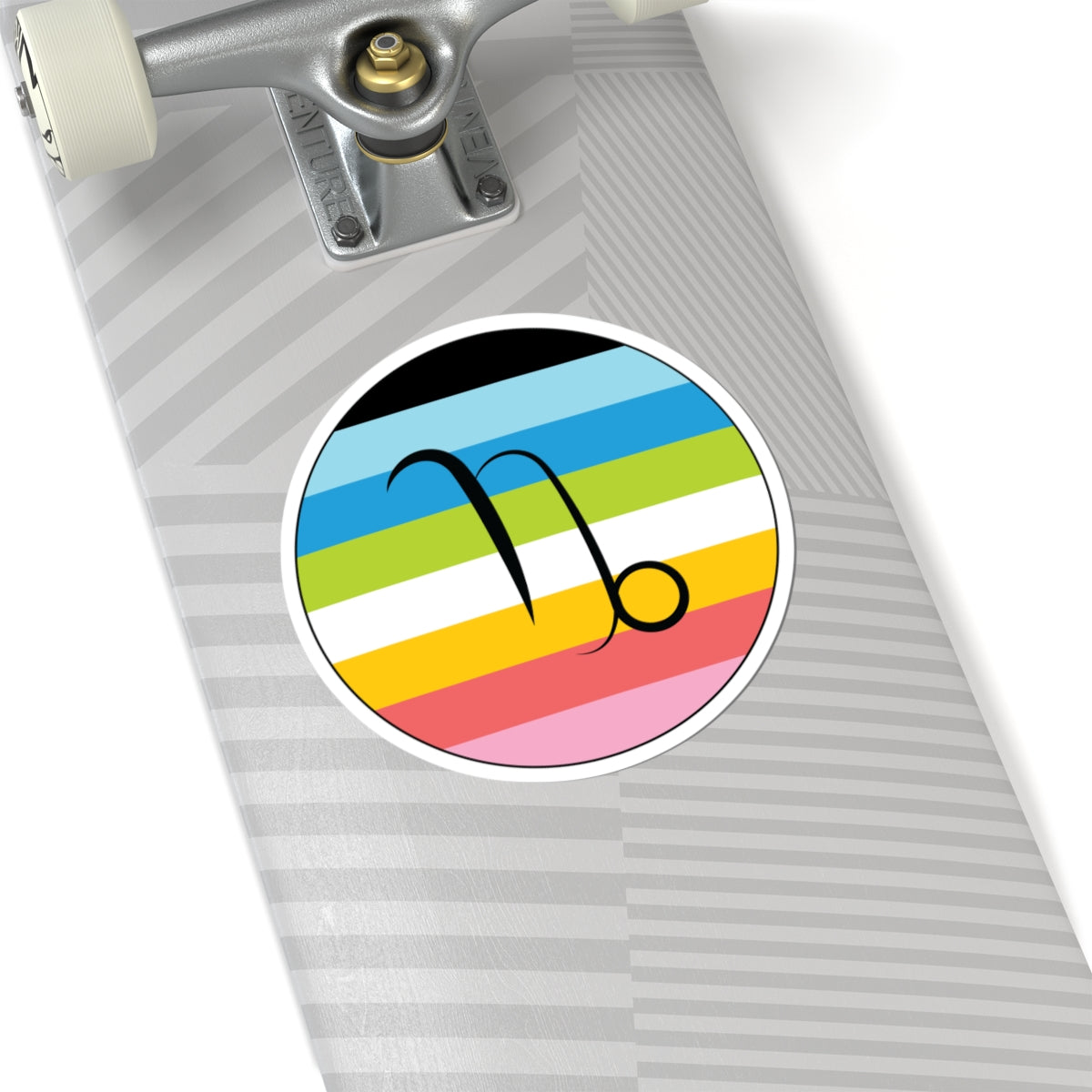 Close-up of the bottom of a silver skateboard featuring a 6 inch by 6 inch circular zodiac sticker with a centered Capricorn glyph on a Queer pride flag style background applied to the surface.