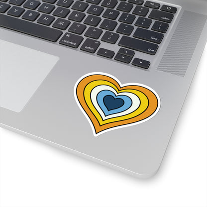 Close-up of the bottom right corner of a silver laptop featuring a 3 inch by 3 inch pride flag heart sticker in an Aroace flag style applied to the surface.