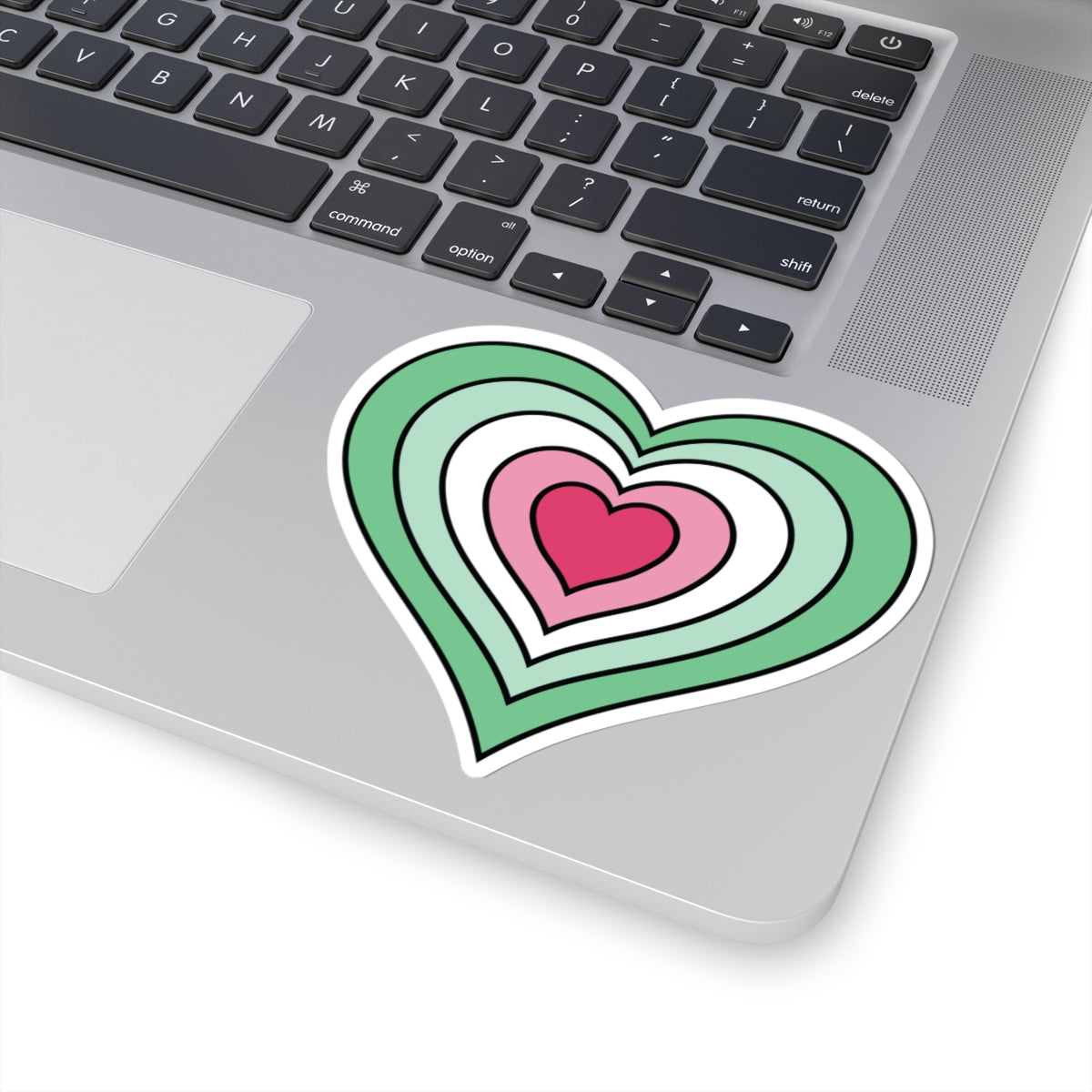 Close-up of the bottom right corner of a silver laptop featuring a 4 inch by 4 inch pride flag heart sticker in an Abrosexual flag style applied to the surface.
