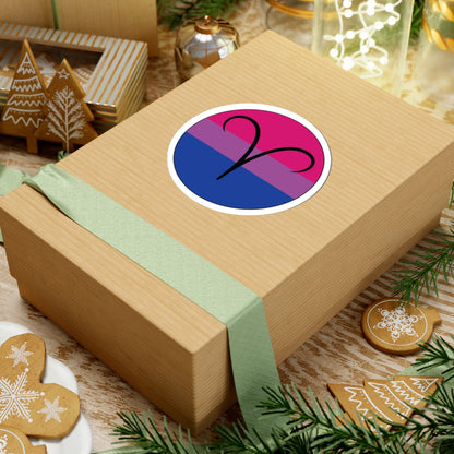 Gift box with a green ribbon on a festive background with cookies and Christmas decorations. Aires Bisexual pride sticker centered on the box.