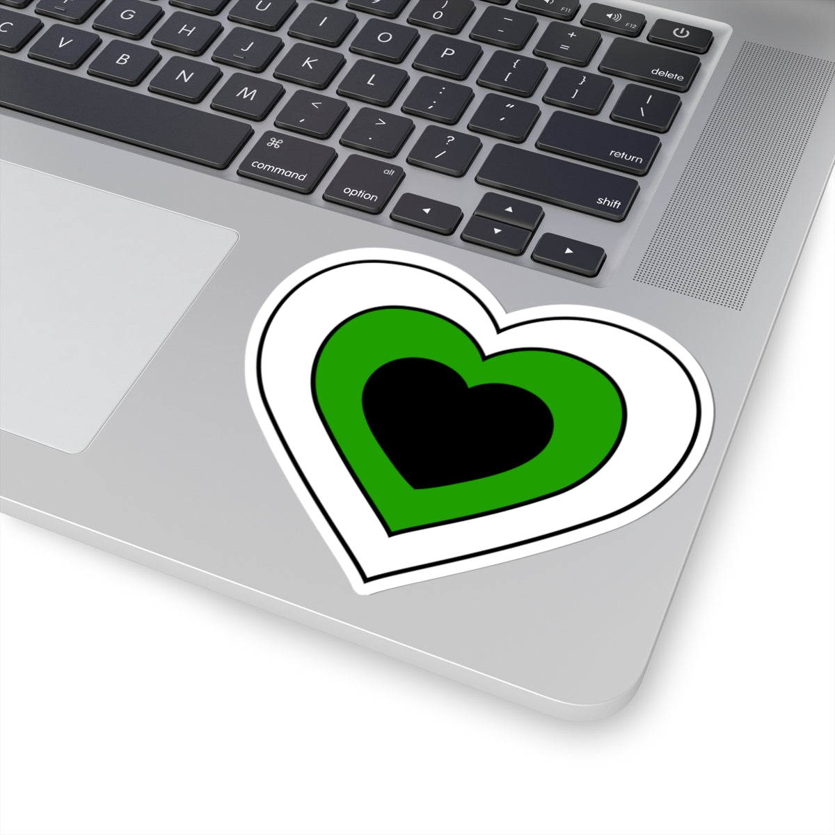 Close-up of the bottom right corner of a silver laptop featuring a 4 inch by 4 inch pride flag heart sticker in a Neutrois flag style applied to the surface.