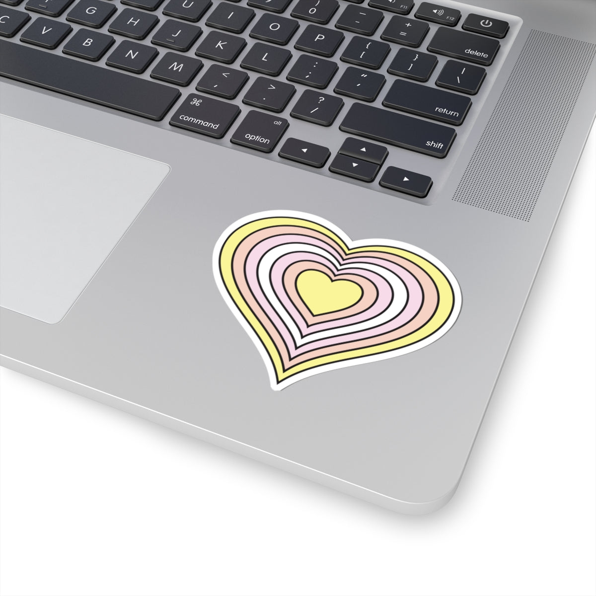 Close-up of the bottom right corner of a silver laptop featuring a 3 inch by 3 inch pride flag heart sticker in a Pangender flag style applied to the surface.