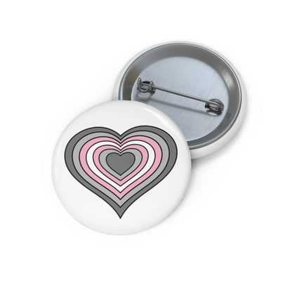 Front and back view of a circular pride button featuring a nested heart design inspired by the demigirl pride flag in gray, light gray, pink, and white. The design has a thin black border, and the button is shown on a white background.