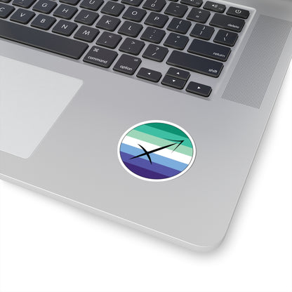 Close-up of the bottom right corner of a silver laptop featuring a 2 inch by 2 inch circular zodiac sticker with a centered Sagittarius glyph on a Gay Men pride flag style background applied to the surface.