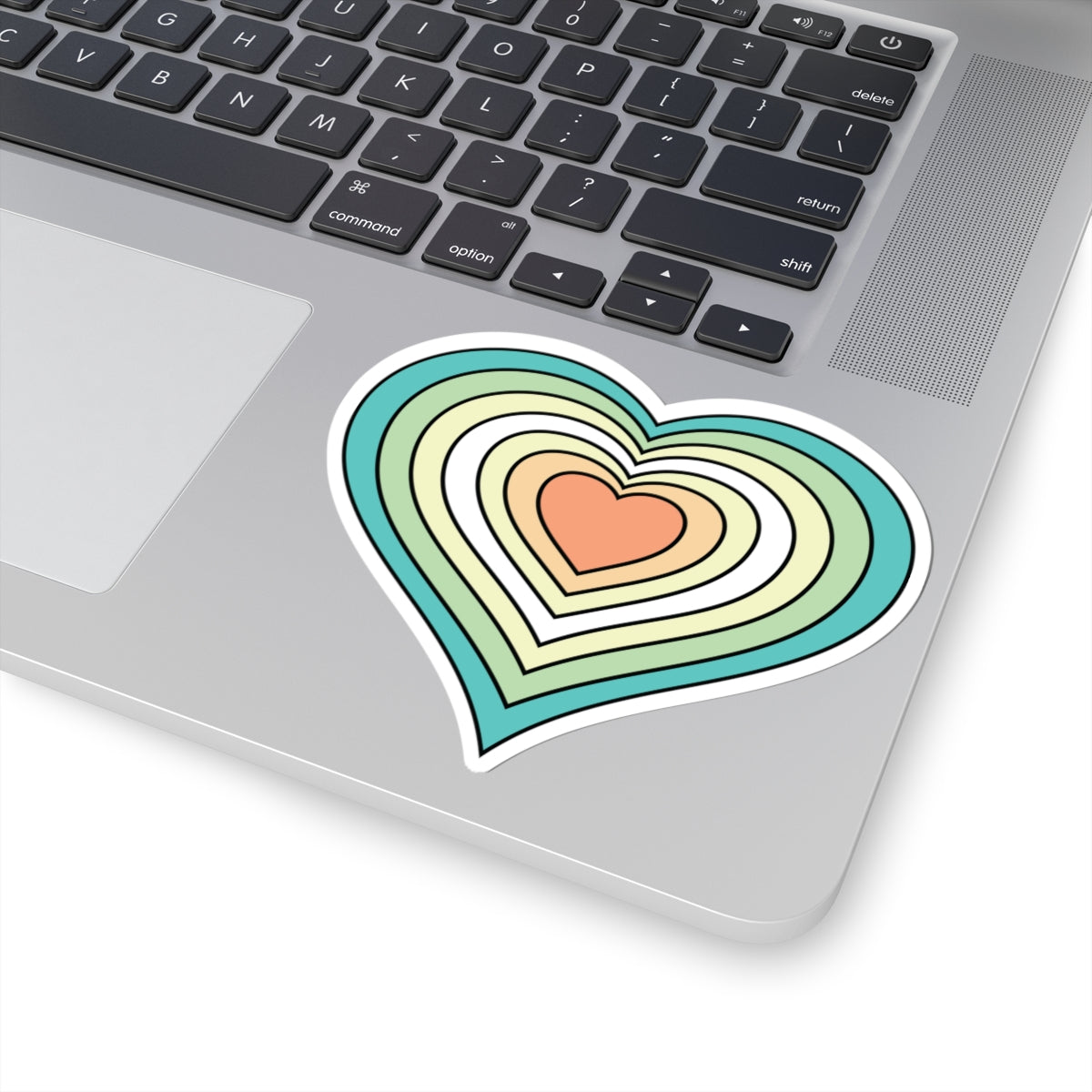 Close-up of the bottom right corner of a silver laptop featuring a 4 inch by 4 inch pride flag heart sticker in a Genderfloren flag style applied to the surface.