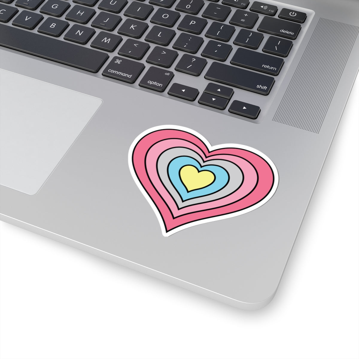 Close-up of the bottom right corner of a silver laptop featuring a 3 inch by 3 inch pride flag heart sticker in a Genderflux flag style applied to the surface.