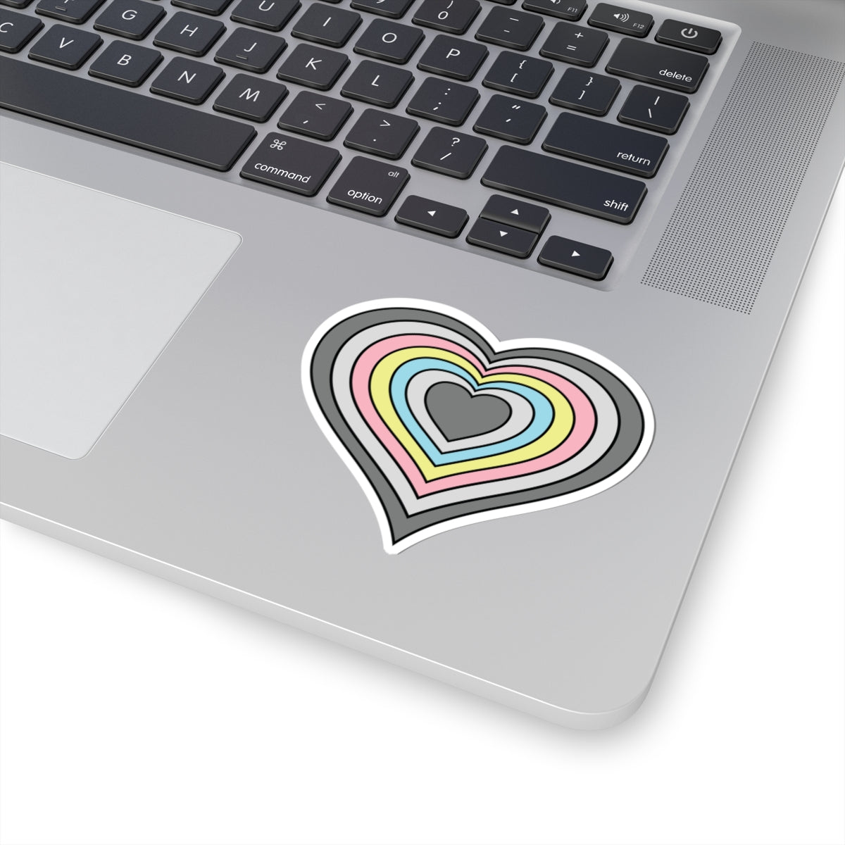 Close-up of the bottom right corner of a silver laptop featuring a 3 inch by 3 inch pride flag heart sticker in a Demiflux flag style applied to the surface.